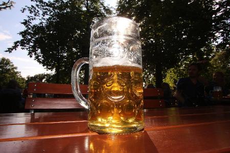 Halbvolle Maß Bier wird vom Sonnenlicht durchleuchtet im Biergarten
