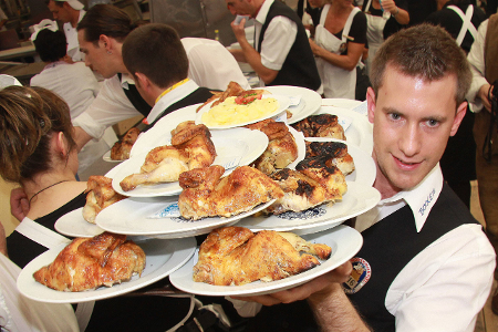 Kellner auf der Wiesn schleppt Teller voll Brathendl