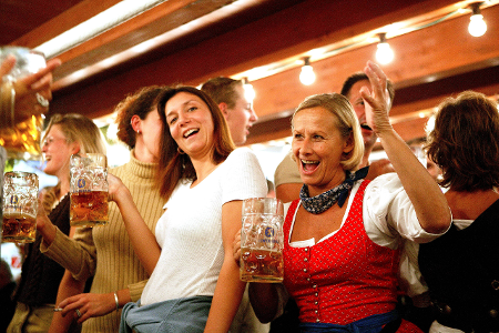 Mehrere Menschen mit Maßkrügen in der Hand singen ausgelassen