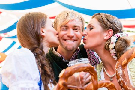 Zwei Frauen busseln einen Mann auf dem Oktoberfest