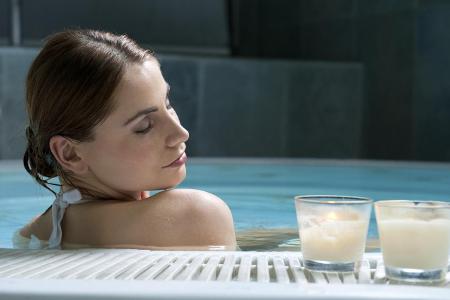 Frau sitzt im Pool neben zwei brennenden Kerzen