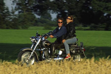 Ein gutaussehendes Paar auf dem Motorrad im Gruenen, Model-R...
