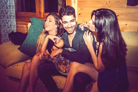 Flirt-Mythen Young women flirting with man while sitting with him on sofa...