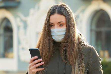 Eine junge Frau mit Schutzmaske und Smartphone. (Symbolbild)