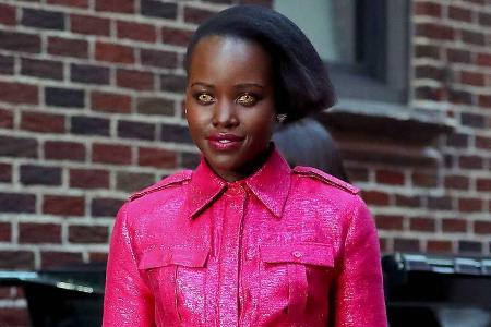 Lupita Nyong'o trägt einen pinken Overall und goldene Kontaktlinsen