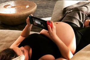 Chrissy Teigen mit Baby-Bauch auf dem Sofa