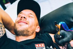 Lukas Podolski mit schmerzverzerrtem Gesicht beim Tätowierer