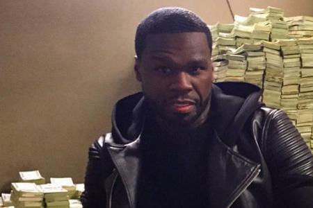 50 Cent sitzt lässig vor einem Berg aus Geldscheinen.