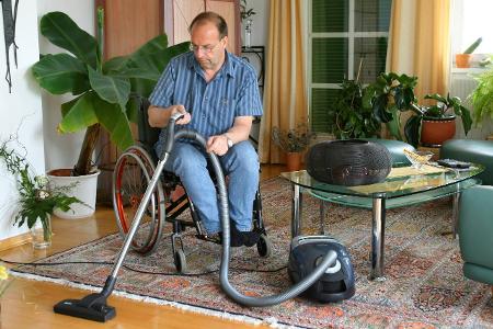 Mann im Rollstuhl saugt in seiner Wohnung man in a wheelchai...