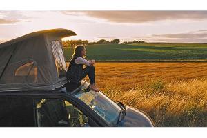 Woman sitting on roof of campervan at sunset