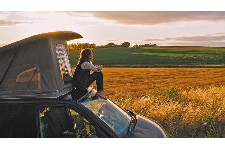 Woman sitting on roof of campervan at sunset