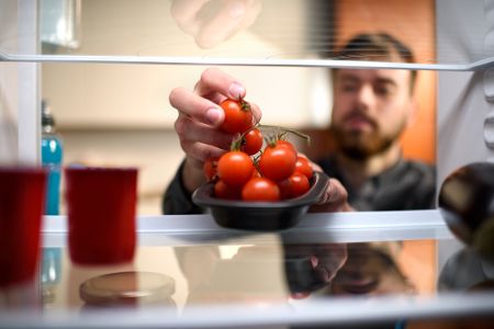 Mann holt sich Tomaten aus einem Kühlschrank