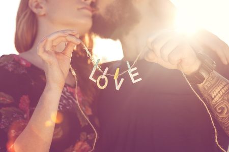 Pärchen hält kleine Girlande mit dem Wort Love und küsst sich