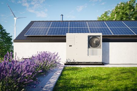 Haus mit Solaranlage und Wärmepumpe, im Hintergrund eine Windkraftanlage.