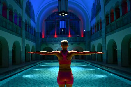 Frau steht mit ausgebreiteten Armen am Beckenrand im Stadtbad Oderberger Straße in Berlin