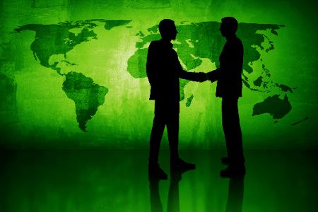 Zwei Menschen geben sich vor einer grünen Weltkarte die Hand
