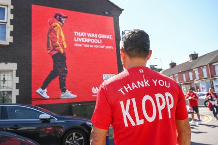 Fan in Klopp-Trikot steht vor Videoleinwand, auf der Jürgen Klopp gedankt wird für 9 Jahre Liverpool.