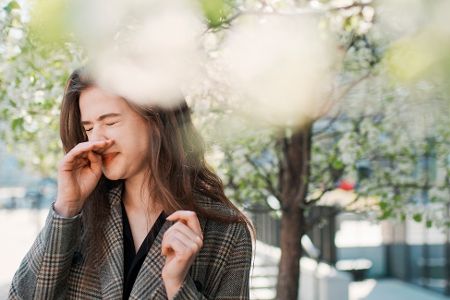Frau niest unter Bäumen mit Pollen