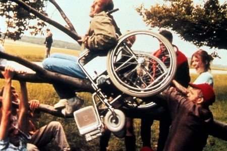 Mann im Rollstuhl hängt in einem Baum umringt von anderen Menschen