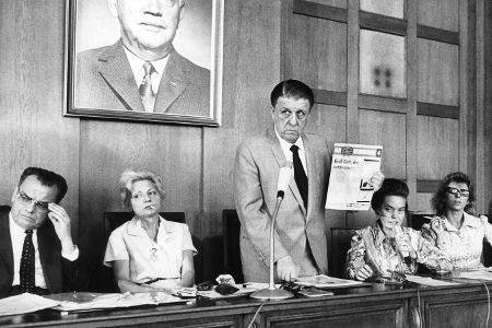 Mann steht in einem Gerichtssaal und hält einen Zettel hoch, schwarzweiß