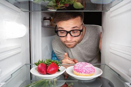 mann hat die wahl zwischen erdbeeren und dounut im kühlschrank
