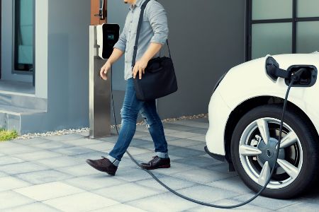 Mann läuft über Ladekabel vom E-Auto