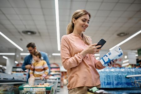 Frau schaut beim Milcheinkauf im Supermarkt auf ihr Handy