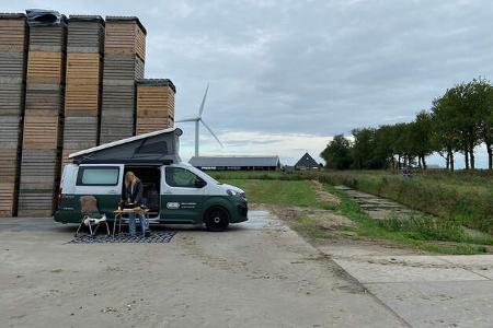 Camper mit Aufstelldach vor einem Windrad