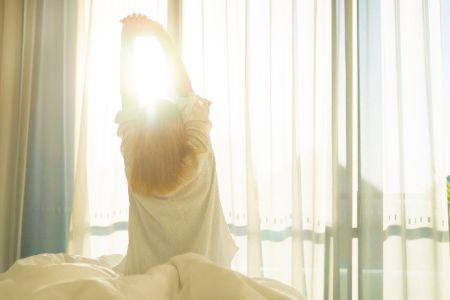 Frau räkelt sich im Bett bei Sonnenschein