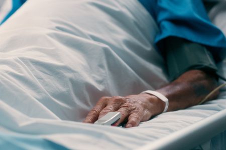 Ältere Person liegt im Krankenbett und hat Anschluss am Finger