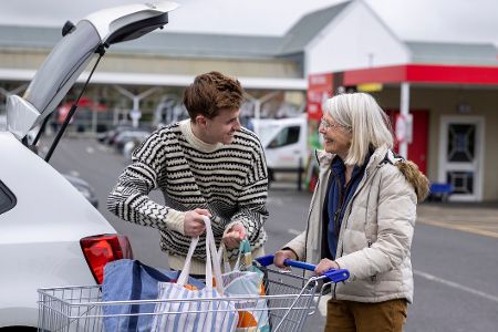 Junger Mann bietet älterer Frau auf dem Supermarktparkplatz an, ihr die Tüten ins Auto zu hieven