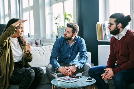 Drei Männer unterhalten sich an einem Couchtisch, die Handys liegen auf dem Tisch.