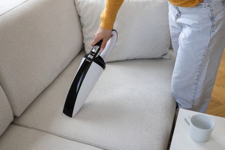 Jemand saugt mit einem Handsauger ein Sofa ab
