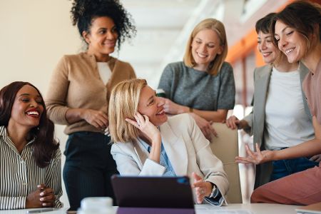 Mehrere Frauen versammeln sich um einen Laptop herum in einem Büro