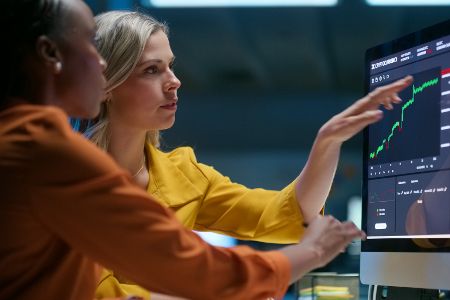 Zwei Frauen schauen sich Börsenkurse auf einem Bildschirm an