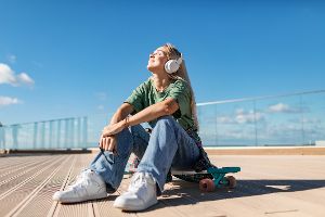 Frau sitzt draußen in der Sonne, hört Musik über Kopfhörer und ist glücklich