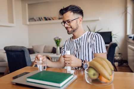 Mann sitzt am Laptop und wirft eine Brausetablette in ein mit Wasser gefülltes Glas