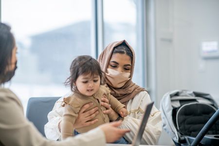 Frau mit Kopftuch und kleinem Kind auf dem Schoß wird beraten