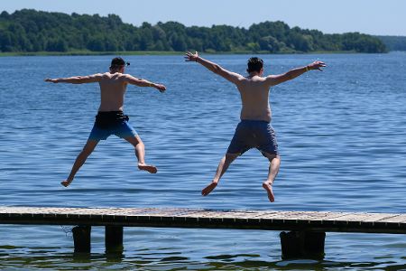 Zwei Jungs springen von einem Steg in einen Badesee