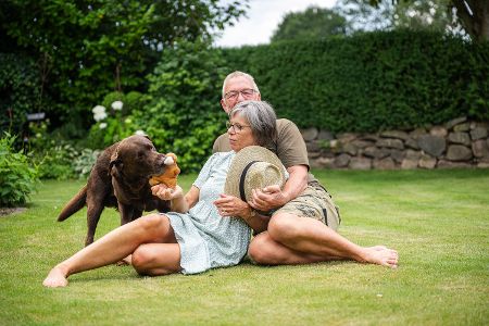 Rentnerpaar sitzt mit Hund auf dem Rasen im Garten