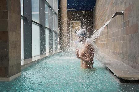 Side view of a man enjoying water massage in a pool under a waterfall jet in health spa