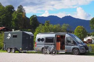 Gray camper van with a horse trailer in a parking lot