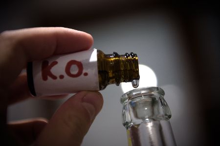 Mensch füllt aus Glasflakon K.o.-Tropfen in eine Flasche.