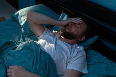 Schlafloser Mann im Bett hält sich den Kopf