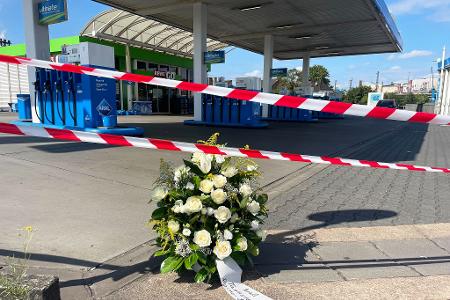 Ein großer Blumenkranz steht vor der überfallenen Tankstelle.