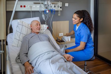 Krankenschwester sitzt am Bett eines Patienten und hält seine Hand
