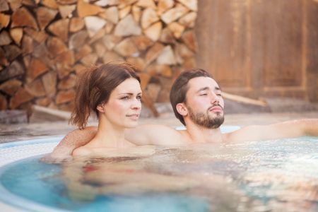 Frau und Mann sitzen in einem Pool vor einem Holzstapel