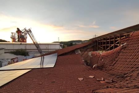 Vom Korb einer Drehleiter heraus kontrolliert ein Feuerwehrmann den eingestürzten Dachbereich.