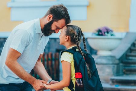 Vater hält die Hände seiner Tochter vor dem Schulgebäude