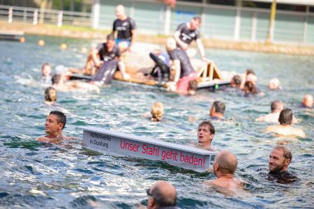 Ein symbolischer Stahlträger mit dem Slogan der Demo schwimmt im Duisburger Innenhafen zwischen zahlreichen Stahlbeschäftigten.
